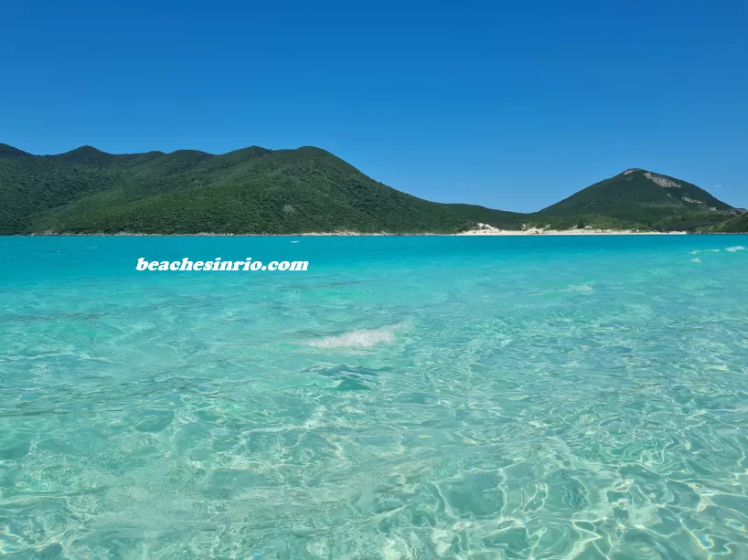 Prainha at Pontal do Atalaia with crystal-clear waters, sunny day, and Farol Island in the background — the Brazilian Caribbean.