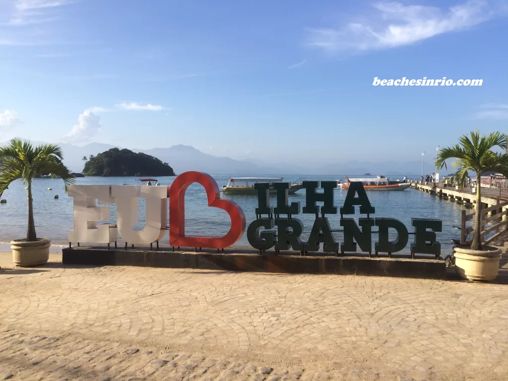 Tourist sign reading 'I Love Ilha Grande' in Vila do Abraão, set against a backdrop of tropical scenery