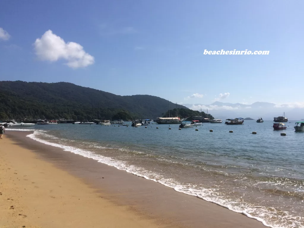 Scenic view of Abraão Beach on Ilha Grande with boats anchored along the shore and lush hills in the background