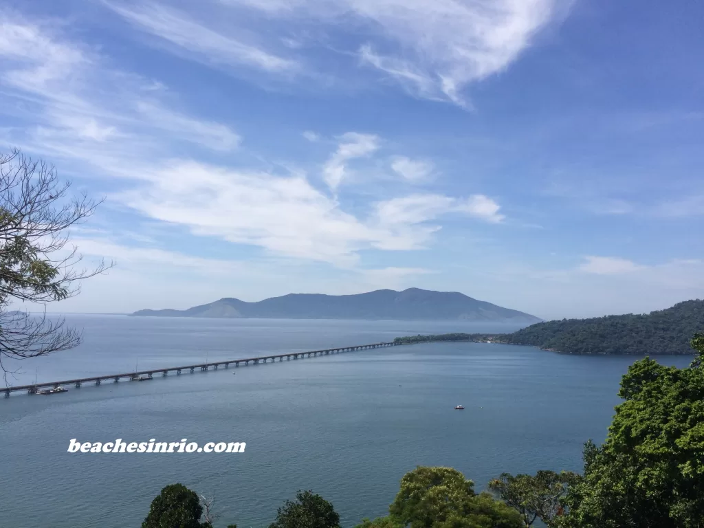 Railway bridge connecting the mainland to Ilha Guaíba, surrounded by lush tropical forest and emerald-green waters.