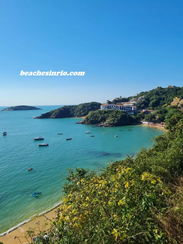 João Fernandes Beach in Buzios, Brazil - Panoramic view from the lookout, showing crystal-clear waters, native vegetation, boats, and bathers, with João Fernandinho Beach visible in the background.
