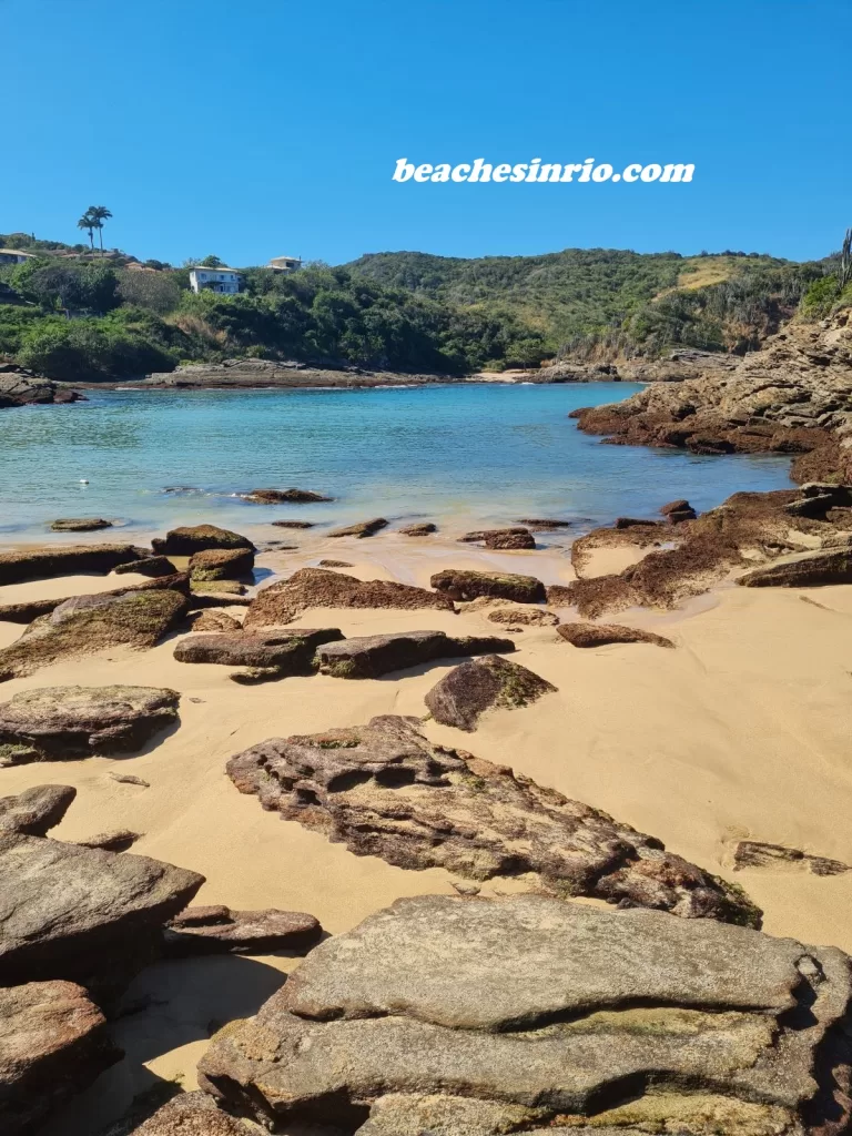Romantic view of Ferradurinha Beach in Buzios, Brazil, on a sunny winter day with calm waters, rocky landscape, and cozy atmosphere.