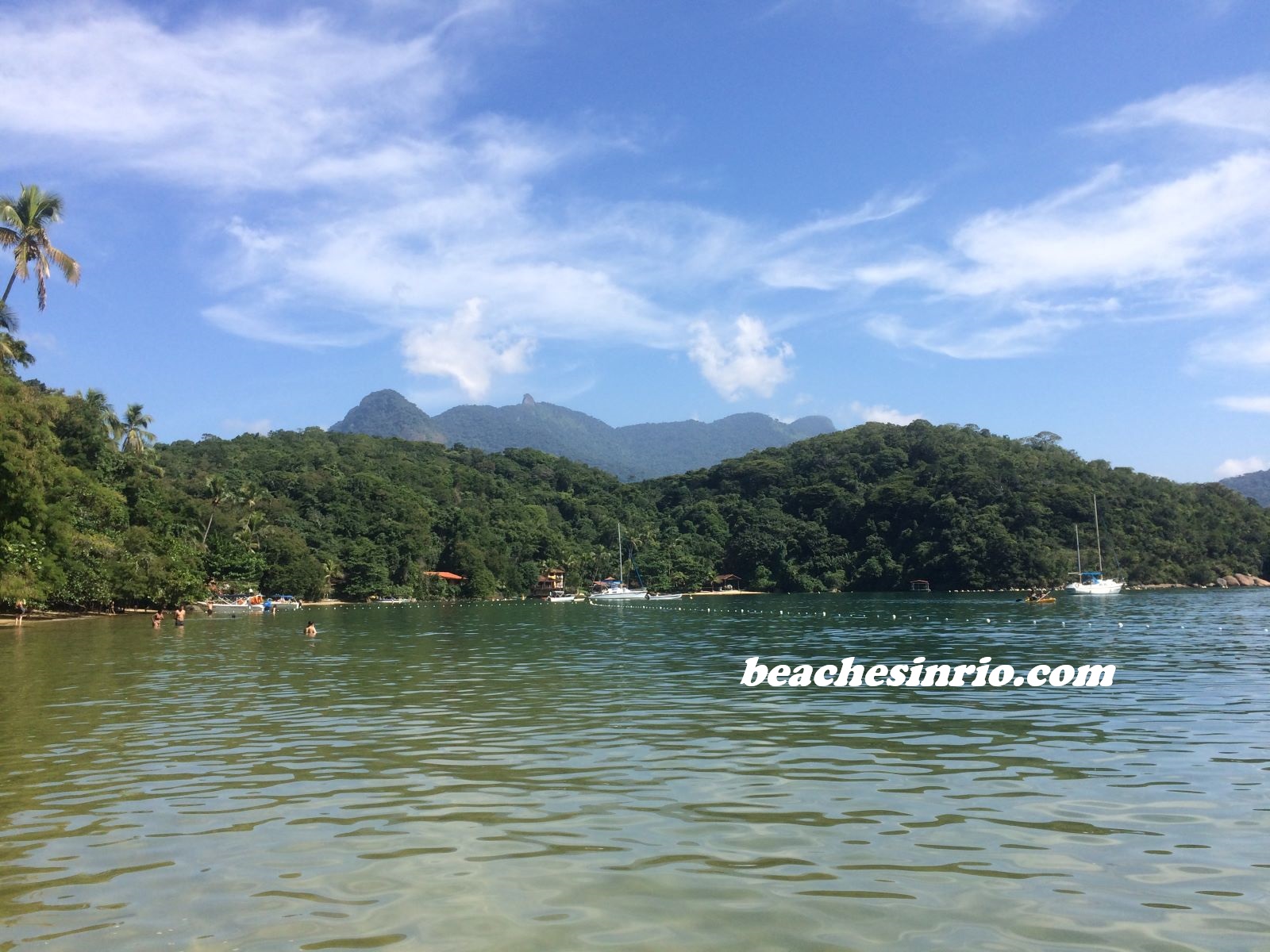 Abraãozinho Beach: Crystal-clear emerald waters with green mountains in the background under a bright sunny sky.